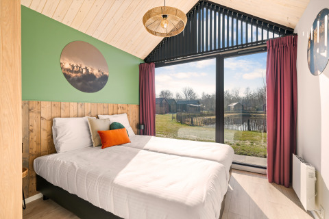 Camera luminosa presso Cosy Lodge, Campeggio Si-Es-An nei Paesi Bassi, con ampia finestra e vista sul lago.