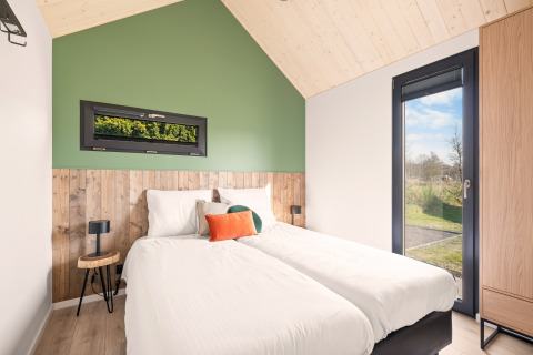Moderne soveværelse i Cosy Lodge på Campingplads Si-Es-An, Nederlandene, med to enkeltsenge og store vinduer.