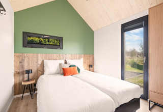 Modern bedroom in the Cosy Lodge at Campsite Si-Es-An, Netherlands, featuring twin beds and large windows.