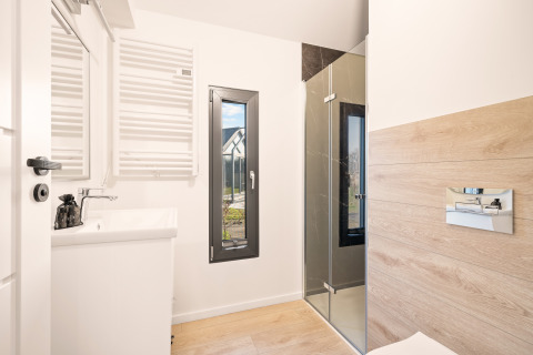 Modern bathroom at Cosy Lodge, Campsite Si-Es-An, Netherlands, featuring shower, sink, window and wood accents.