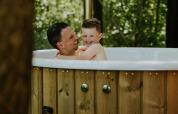 Un padre felice e suo figlio si godono una vasca idromassaggio insieme presso Happy bee lodge al campeggio Si-Es-An nei Paesi Bassi.