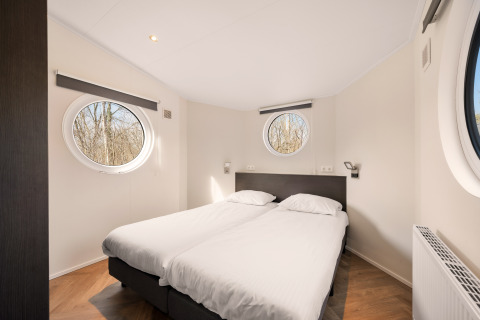 Dormitorio moderno con dos camas individuales y ventanas redondas en Happy bee lodge, Camping Si-Es-An, Países Bajos.