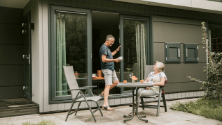 Oudere koppel geniet van koffie aan een tafeltje voor een tiny house genaamd Luxury Loft in de tuin.