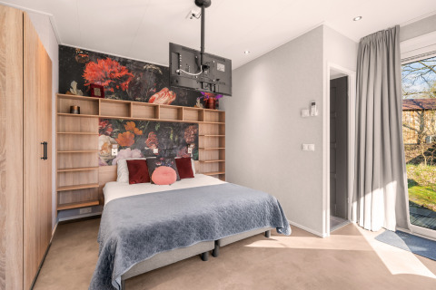 Moderne tiny house soveværelse med blomstret væg, trægarderobe og tv ved Campsite Si-Es-An i Holland.