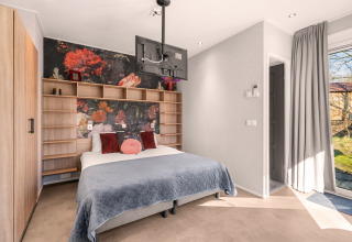 Moderne tiny house soveværelse med blomstret væg, trægarderobe og tv ved Campsite Si-Es-An i Holland.