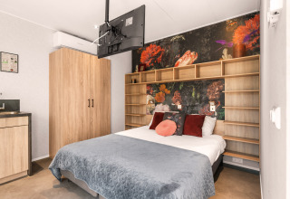 Loft de luxe tiny house au camping Si-Es-An, Pays-Bas, avec lit moderne et fresque murale florale colorée.