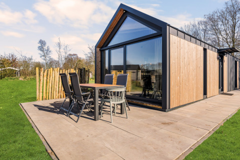 Moderne Reestdal lodge med træpaneler og store glasvinduer, udendørs terrasse med bord og stole.
