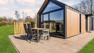 Modern Reestdal lodge with wooden paneling, large glass windows, and patio seating on a spacious terrace.