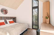 Modern bedroom at the Reestdal lodge, Campsite Si-Es-An, Netherlands, with wood ceiling and tall windows.