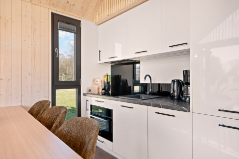 Cucina moderna con mobili bianchi e finestra alta nel lodge Reestdal al campeggio Si-Es-An, Paesi Bassi.