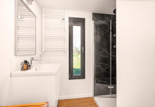 Moderne badeværelse i "Reestdal"-lodge på Campsite Si-Es-An i Holland, med bruser, vask og vindue.