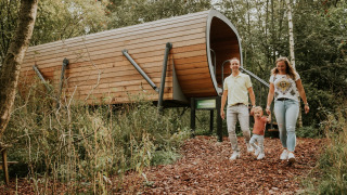 Gezin verlaat het Skycabin natuurhuisje, loopt over een bladerpad omgeven door bomen en natuur.