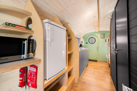 Interior of a cozy nature house with kitchen, fridge, microwave, and green door at Campsite Si-Es-An, Netherlands.