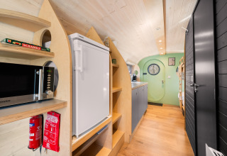 Interieur van een knus natuurhuisje met keuken, koelkast, magnetron en groene deur op Campsite Si-Es-An.