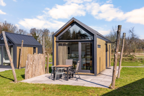 Tiny house moderna con rivestimento in legno, ampie finestre e area salotto esterna su prato verde.