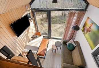 Oversigtsbillede af en hyggelig tiny house med store vinduer, sofa, spisebord og tv på Campsite Si-Es-An.