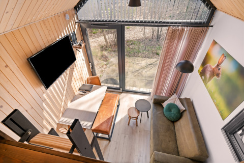 Vista desde arriba de una tiny house acogedora en Si-Es-An, con sofá, mesa, televisor y ventanales.