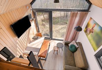 Vista dall’alto di una tiny house accogliente al Si-Es-An con divano, tavolo, TV e grandi finestre.
