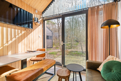 Bright living area inside a tiny house at Campsite Si-Es-An, Netherlands, with large windows and forest view.