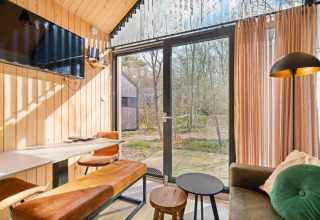 Bright living area inside a tiny house at Campsite Si-Es-An, Netherlands, with large windows and forest view.