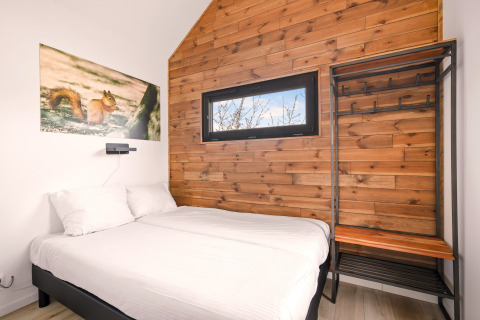 Dormitorio en una tiny house en el Camping Si-Es-An, Países Bajos, con pared de madera y cama cómoda.