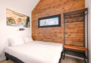Camera da letto in tiny house al Campeggio Si-Es-An, Paesi Bassi, con parete in legno e letto accogliente.