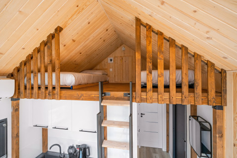 Cozy wooden loft with beds above a small kitchen in a tiny house at Campsite Si-Es-An in the Netherlands.