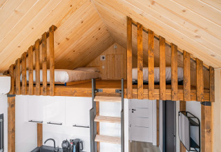 Ático de madera con camas sobre una cocina pequeña en tiny house del camping Si-Es-An, Países Bajos.