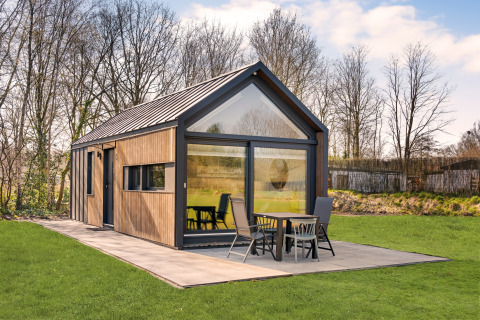 Modern lodge called Reestdal Loft with large windows and patio, set amidst green grass and surrounding trees.