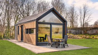 Moderno lodge chiamato Reestdal Loft con ampie vetrate e patio, immerso nel verde e circondato da alberi.