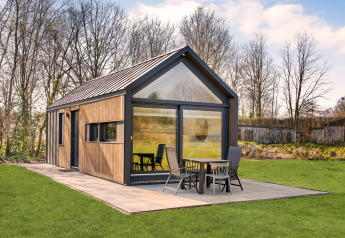 Moderno lodge chiamato Reestdal Loft con ampie vetrate e patio, immerso nel verde e circondato da alberi.