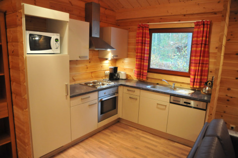 Cuisine moderne au chalet ‘De Boshut’ en Belgique avec électroménagers, murs en bois et une grande fenêtre.