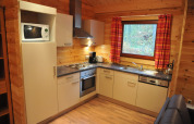 Modern kitchen in ‘De Boshut’ chalet, Belgium, featuring appliances, wood walls, and a large window.