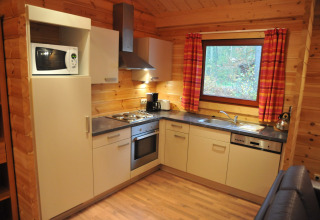 Cuisine moderne au chalet ‘De Boshut’ en Belgique avec électroménagers, murs en bois et une grande fenêtre.