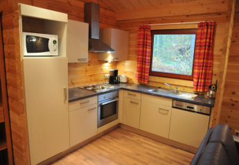 Modern kitchen in ‘De Boshut’ chalet, Belgium, featuring appliances, wood walls, and a large window.
