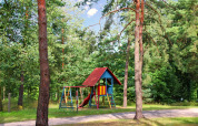 Parque infantil con columpios y tobogán entre árboles junto a Bungalow '50 qm 5 Pers' en Alemania.