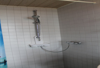 Moderne douche met witte tegels en verstelbare douchekop, gefotografeerd bij lodge «Am Strand» in Duitsland.