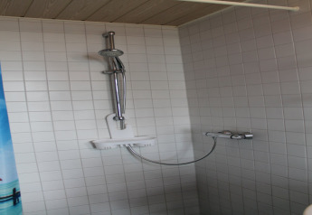 Modern shower with white tiles and adjustable showerhead, photographed at the lodge «Am Strand» in Germany.