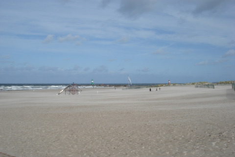 Uitzicht op het brede zandstrand bij lodge 'Am Strand' in Duitsland met zee, speeltuin en vuurtorens.