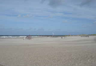 Uitzicht op het brede zandstrand bij lodge 'Am Strand' in Duitsland met zee, speeltuin en vuurtorens.