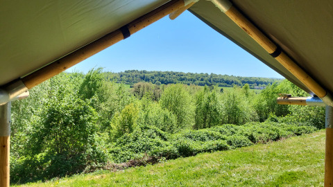 Uitzicht vanuit een safaritent op Camping La Colline in België, met groene natuur en heuvels.