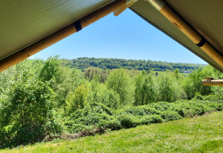 Blick aus einem Safarizelt auf dem Campingplatz La Colline in Belgien mit grüner Natur und Hügeln.