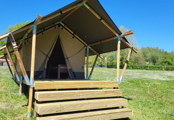 Tenda safari con veranda in legno al campeggio La Colline in Belgio, posizionata su un prato sotto cielo sereno.