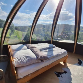 Glamping accommodation at Terrassencamping Schlierbach – Domes Hessen, bed in glass dome with scenic landscape view.