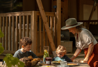 Familia desayuna en una mesa de madera frente a la tienda safari De Stille Heide con estufa y jacuzzi.