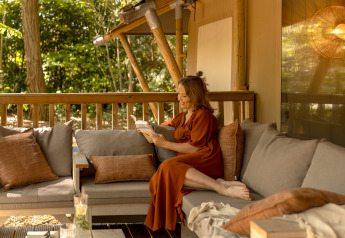Frau liest entspannt ein Buch auf der Terrasse des Safari-Zeltes „De Stille Heide“, Gooise Heide.