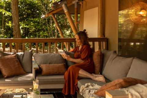 Kvinde læser en bog på terrasse i safari teltet 'De Stille Heide', Gooise Heide, Nederlandene.