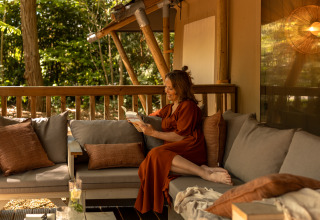 Kvinde læser en bog på terrasse i safari teltet 'De Stille Heide', Gooise Heide, Nederlandene.
