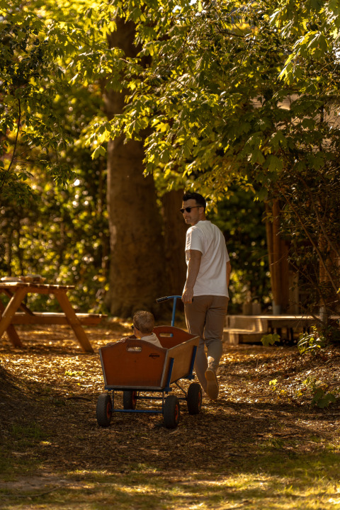 Ein Mann zieht ein Kind in einem Wagen durch den Wald beim Safari-Zelt De Bos Tent in Gooise Heide.