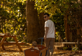 Un hombre tira de un niño en un carro por un sendero boscoso en la tienda safari De Bos Tent en Gooise Heide.